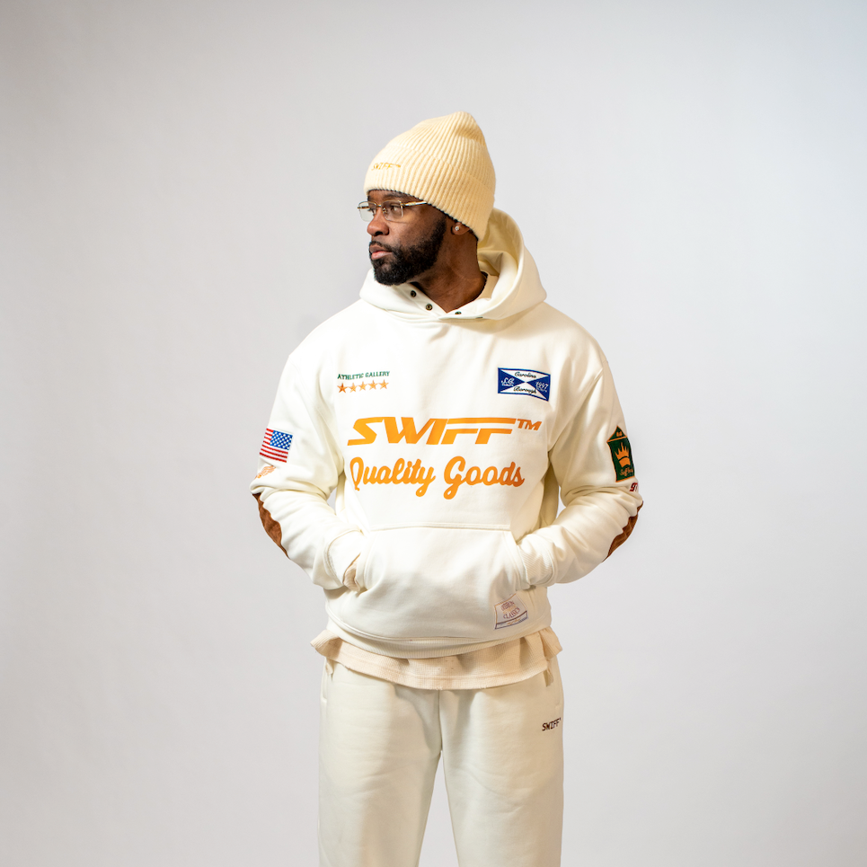 Person wearing a cream-colored hoodie with branding on a gray background