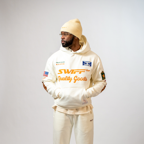 Person wearing a cream-colored hoodie with branding on a gray background